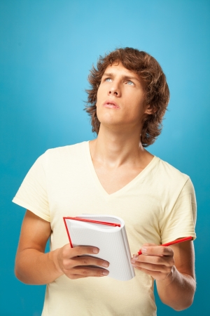 Worried young man holding a notebook and looking up.の写真素材