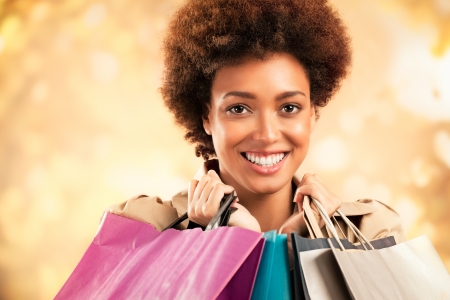 Stylish African-American woman posing in front of a glittering gold background ang holding shopping bags.の写真素材