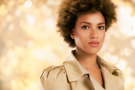 Stylish African-American woman posing in front of a glittering gold background.の写真素材