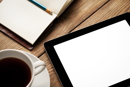 Digital tablet, a cup of coffee and an open agenda on a wooden table.の写真素材