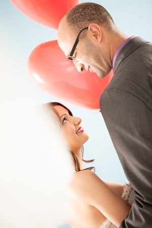 Smiling bride and groom looking at each other and holding heart-shaped balloons.の写真素材