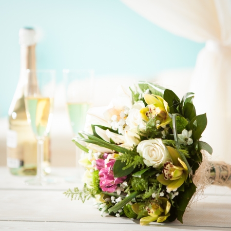 Colourful wedding bouquet in front of a bottle of champagne and two flutes for the newlyweds.の写真素材