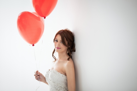 Beautiful young bride standing against the wall and holding heart-shaped balloons.の写真素材