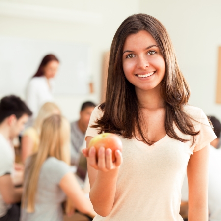 Smiling college student holding an apple and standing in front of her peers.の写真素材