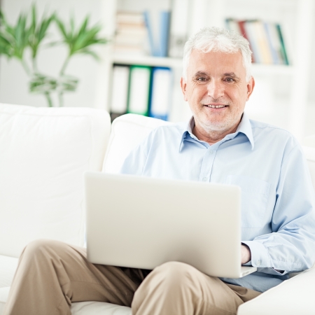 Smiling senior man sitting in his living room and using his laptop.の写真素材