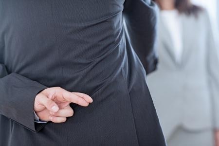 Business partners shaking hands with one of them holding her fingers crossed behind her back.の写真素材