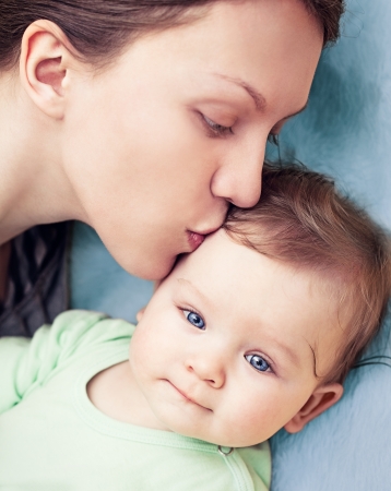 Baby boy with beautiful blue eyes being kissed by his mother の写真素材