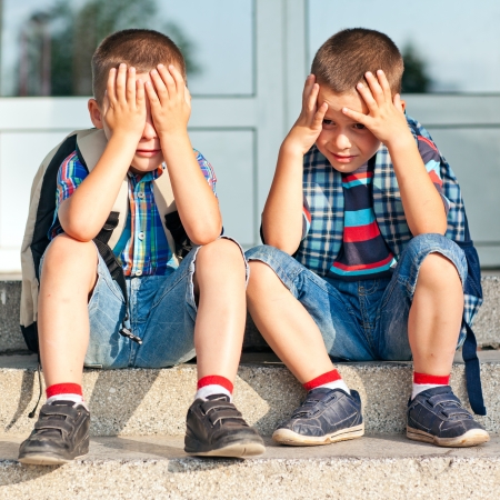 Two worried schoolboys sitting in front of their school.の写真素材