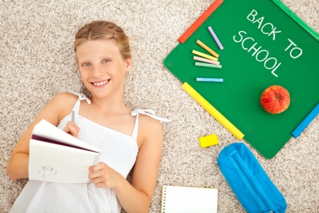 A smiling schoolgirl lying on the floor and doing homework at home.の写真素材