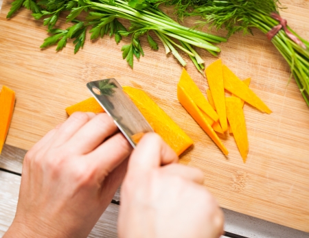 Female hands cutting carrots on a wooden board.の写真素材