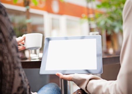 Two women using a tablet while having coffee at a sidewalk cafe.の写真素材
