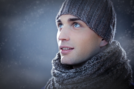 Handsome young man wearing a knit hat and a scarf looking up.の写真素材