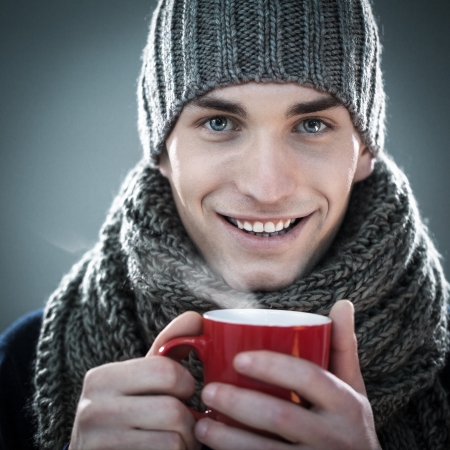 Handsome young man in winter clothes holding a cup of hot tea.の写真素材