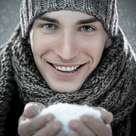 Handsome young man holding snow in his hands.の写真素材