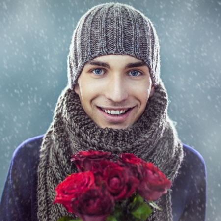 Handsome young man in winter clothes holding a bunch of red roses.の写真素材