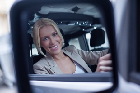 Beautiful mid-adult woman driving her car looking at her reflection at the rear-view mirror.の写真素材