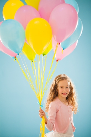Cute smiling girl holding a bunch of colourful balloons.の写真素材