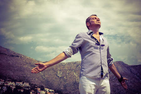 Carefree man enjoying in freedom with arms outstretched. Below view of man breathing fresh air with eyes closed.の写真素材