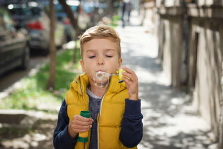 Little boy with bubble wand blowing soap bubbles on the street.