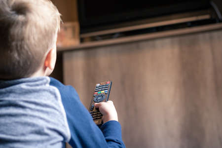 Kid watching TV and changing channels with remote control.の写真素材