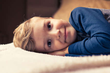 Cute kid relaxing on a bed and looking at camera.