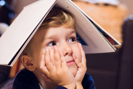 Close up portrait of small boy holding book on his head.