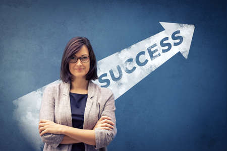 Confident businesswoman with crossed arms standing in front of a wall with success arrow sign.の写真素材
