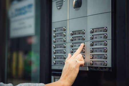 Close up of woman using intercom at residential building entrance.