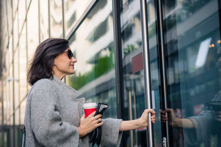 Smiling woman entering in residential building. Happy businesswoman coming to work and entering in...
