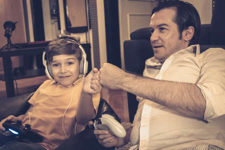 Happy boy fist bumping with his father while playing video games at home.