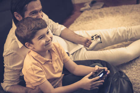 Happy son and father having fun while playing video games together at home.