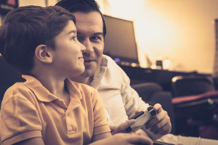 Happy boy and his father communicating while playing video games and having fun at home.