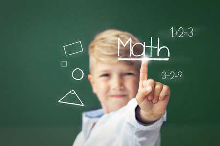 Schoolboy learning mathematics and using digital touch screen in front of blackboard.の写真素材