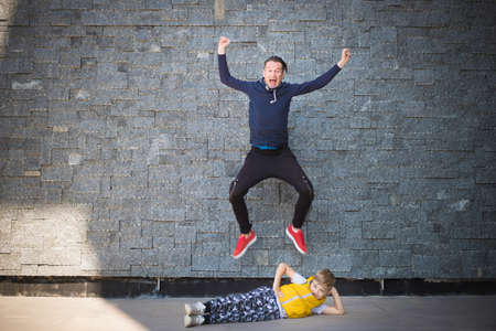 Small kid lying down on the floor and ignoring his father who is jumping with arms raised behind him. Copy space.の写真素材