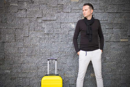 Portrait of mid adult man with yellow travel bag against the wall. Copy space.の写真素材