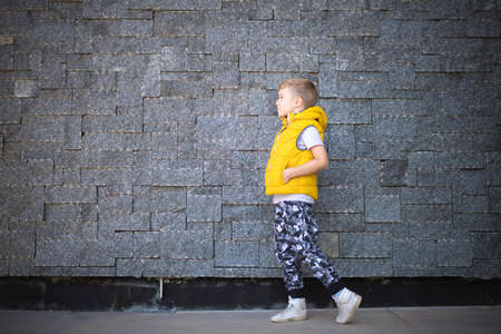 Full length of small boy walking with hands in pockets against the wall. Copy space.