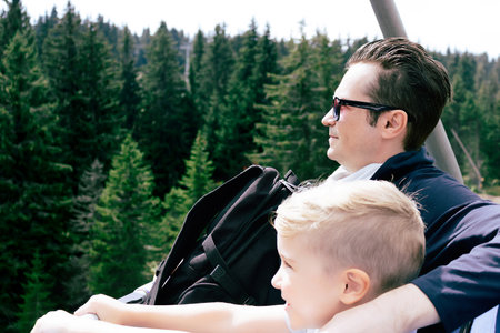 Happy little boy and his father riding on ski lift above the forest in summer day.の写真素材