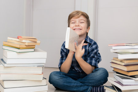 Cute happy kid sitting in between stack of books and looking at camera.の写真素材