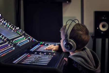 Kid with headphones adjusting volume on audio mixer in recording studio.の写真素材