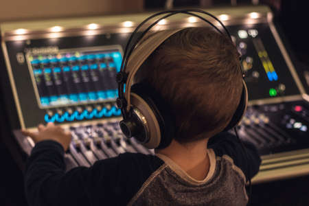 Back view of little DJ with headphones editing music on sound mixer in music studio.の写真素材