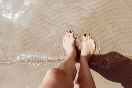 High angle view of barefoot woman standing in shallow water on sandy beach. Copy space.の写真素材