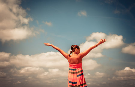 Rear view of woman having fun in summer day while standing with arms outstretched against the sky.の写真素材