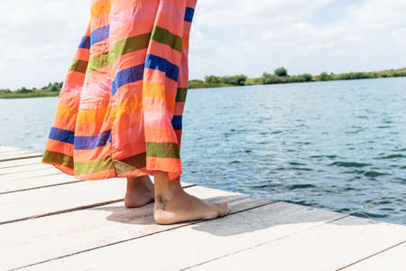 Unrecognizable woman standing on pier by the water in summer day.