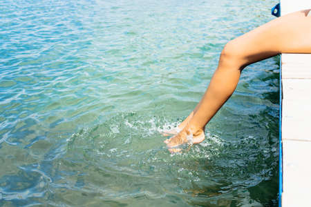 Unrecognizable woman's legs splashing water. Close up of woman on pier at the sea.の写真素材