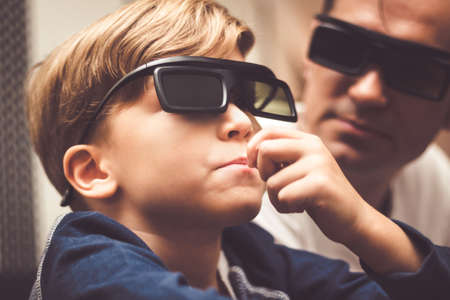 Close up of kid with 3d glasses watching movie with his dad and eating popcorn.の写真素材