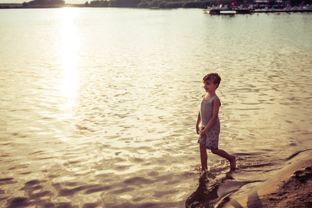 Happy little boy having fun while spending summer day at the beach at sunset.の写真素材