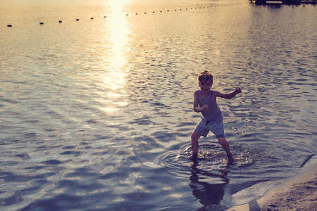 Happy kid dancing in the water at sunset and having fun during summer holiday at the beach.の写真素材