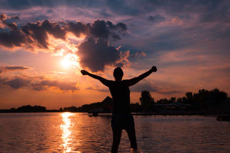 Silhouette of carefree woman with arms outstretched enjoying in freedom and summer at sunset.