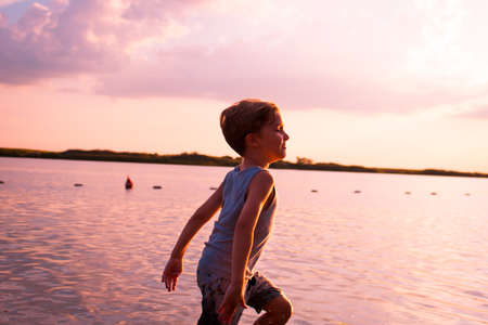 Happy kid running through sea water and having fun at sunset.の写真素材