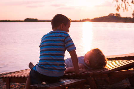 Two boys spending summer holiday at beach and relaxing on deck chairs at sunset.の写真素材